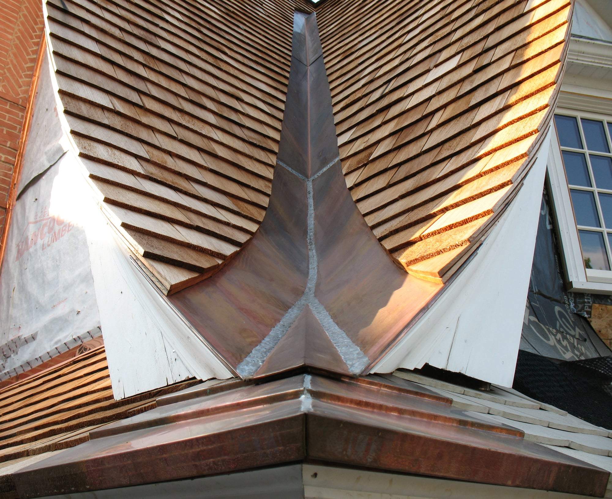 A copper-lined roof valley sweeping between two wood-shingle roof planes.